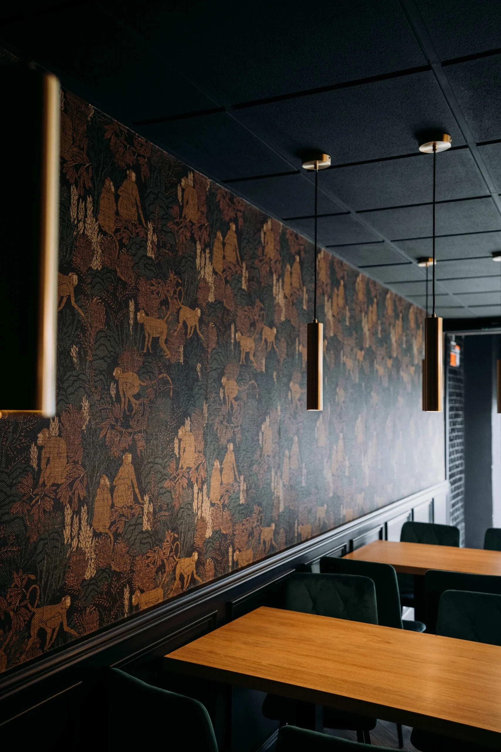 Comedor con techo negro, mesas de madera, y pared de estampado selvático