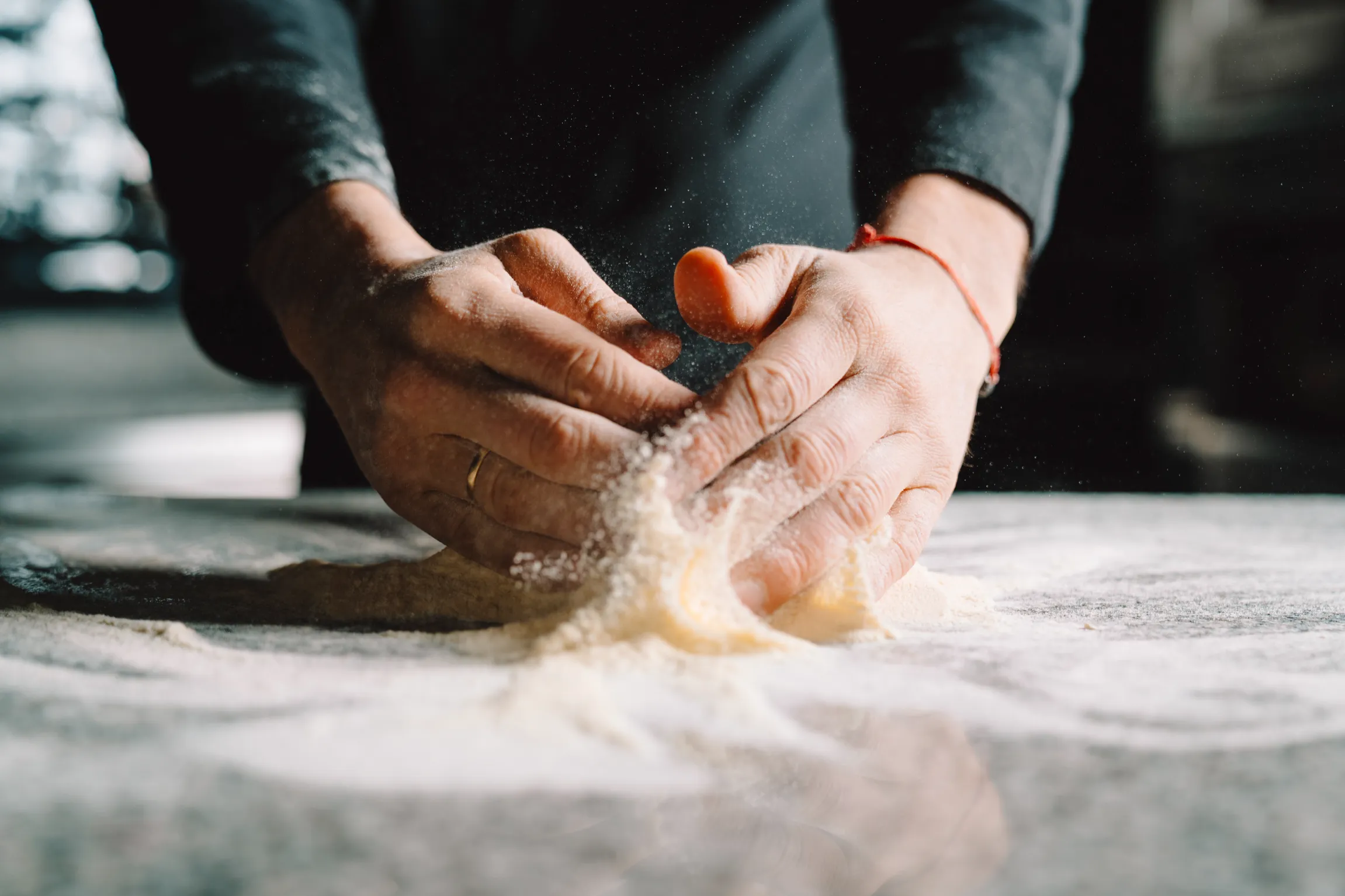 Manos de Pedro moldeando una bola de masa fresca sobre mesa de granito enharinada.