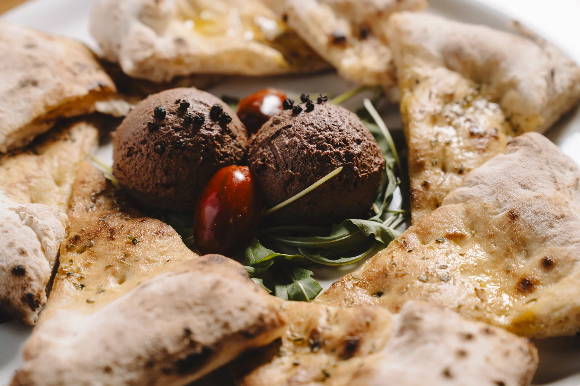 Raciones de piadina artesanal acompañadas de dos bolas de paté casero decorado con granos de pimienta negra sobre cama de rúcula y tomates cherry.