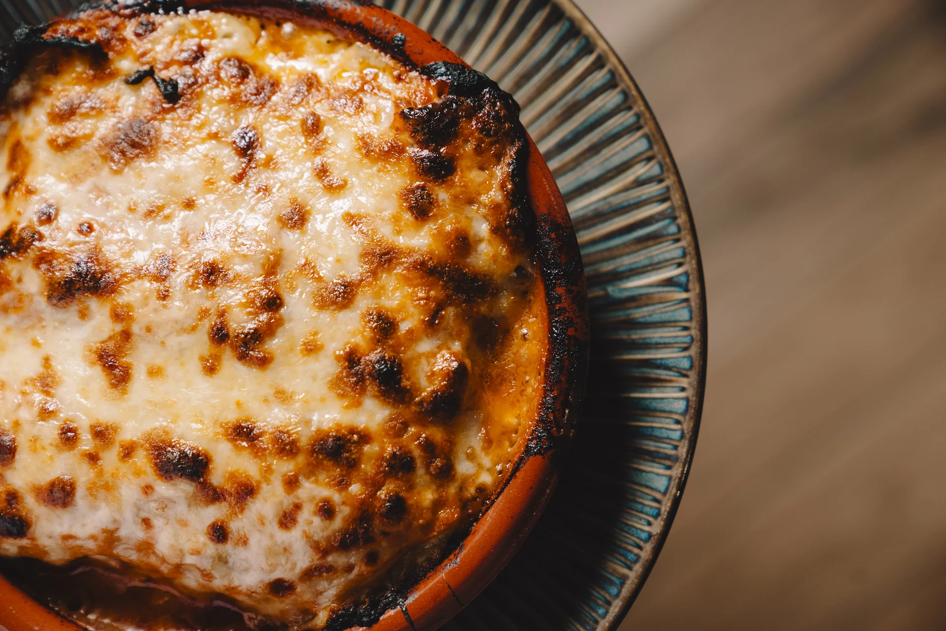 Primer plano cenital de lasaña gratinada con capa de queso fundido y bordes crujientes en cuenco de barro.